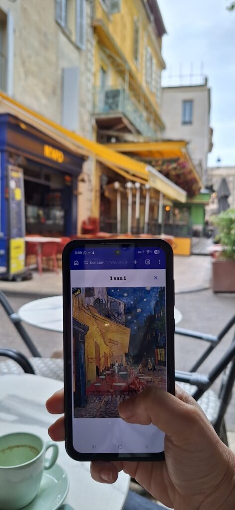 Celular mostrando a pintura Terraço do Café à Noite de Van Gogh em frente ao Café Van Gogh, em Arles
