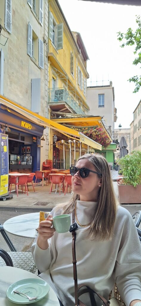 Mulher tomando café na varanda do Café Van Gogh em Arles, com prédios amarelos ao fundo